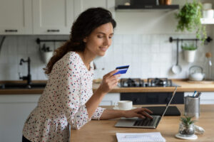 Smiling Caucasian female buyer shopping online on computer from home pay with credit card.